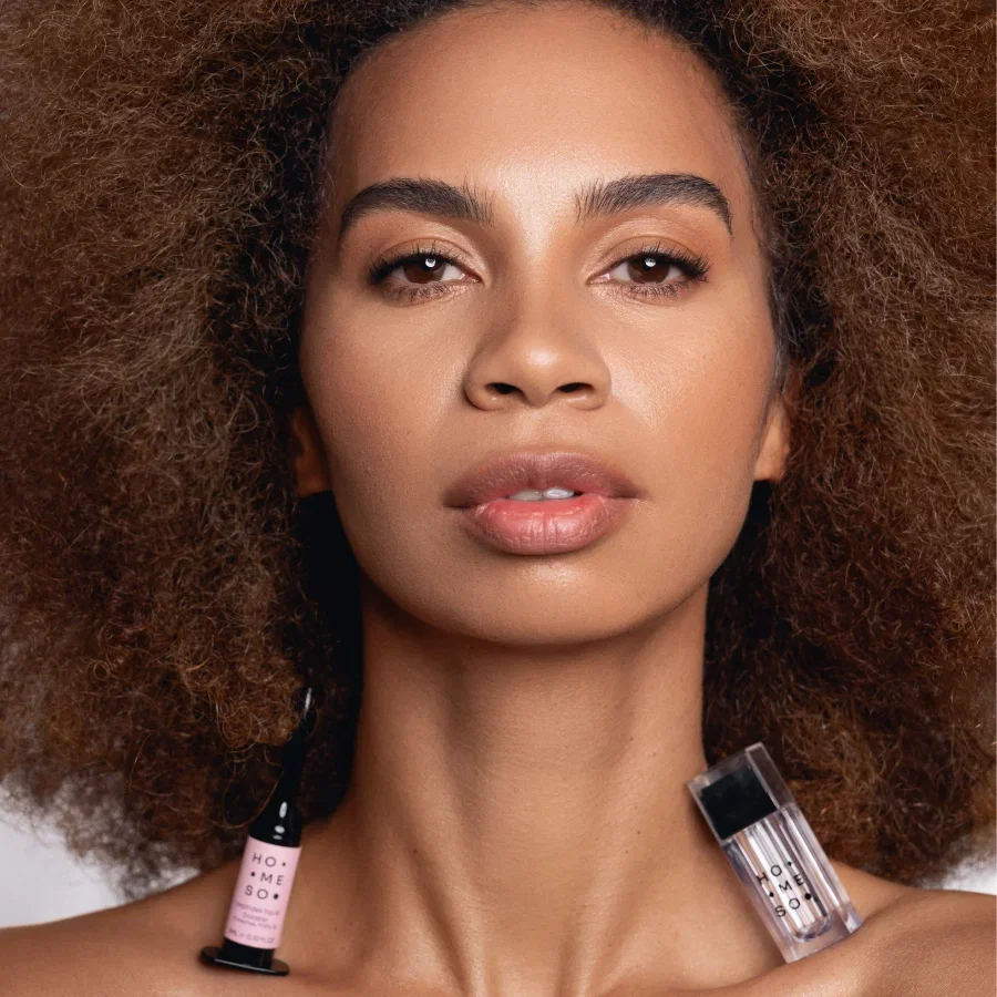 Kvinde med HoMEso microneedling-pen og serum hvilende på skuldrene, strålende hud.